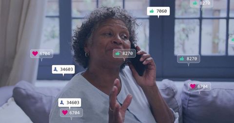 Senior woman talking on smartphone on sofa receiving social media likes and followers