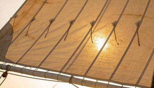 Backlit canvas sail with reinforced seams, tie straps, boom and rigging creating warm glow