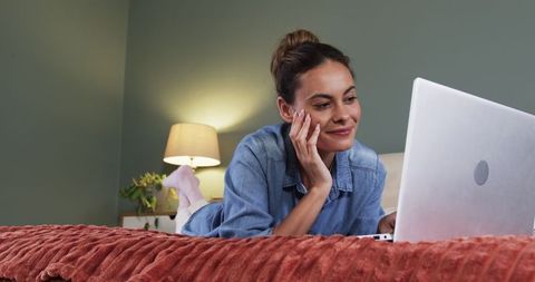 Woman Relaxing on Bed While Using Laptop in Cozy Bedroom