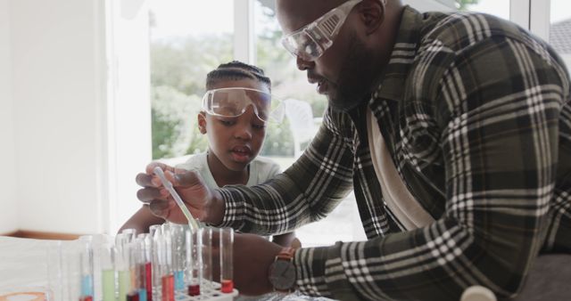 African american father and son sitting at table doing chemistry experiments at home. Family, fatherhood, togetherness, science and domestic life, unaltered.