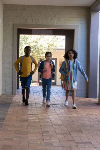 Three schoolchildren walking through brick corridor with backpacks returning to class