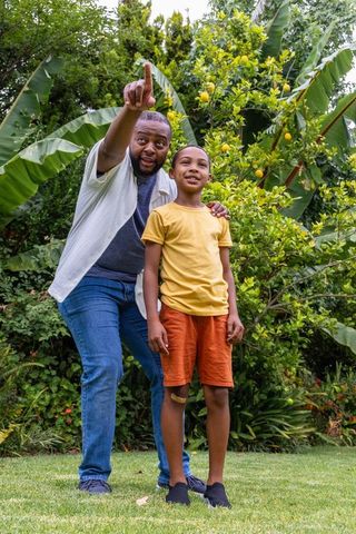 Father pointing to fruit-bearing tree while son looks on in lush backyard garden