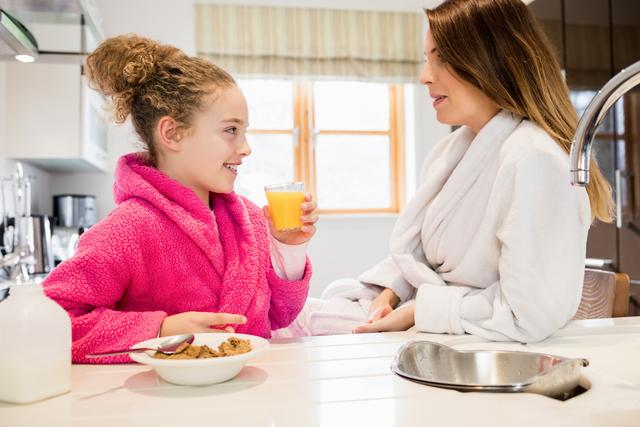 Mother and daughter interacting with each other while having breakfast in kitchen at home