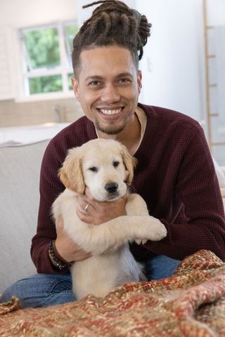 Smiling man cradling golden retriever puppy on sofa in cozy living room
