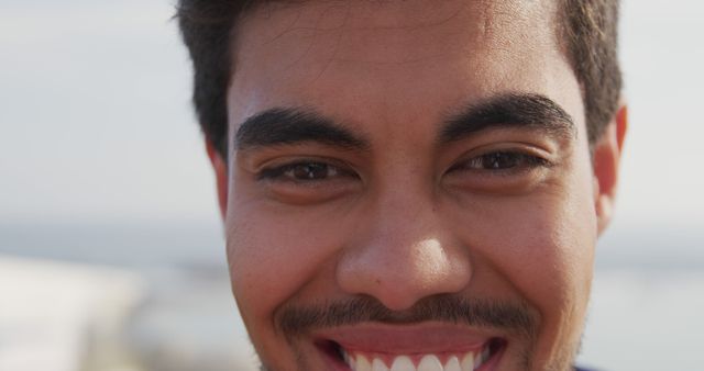 Close-up of young man smiling outdoors with a joyful expression. Ideal for illustrating themes of happiness, positivity, and friendly interactions. Perfect for use in advertisements, social media, mental health campaigns, or lifestyle blogs.