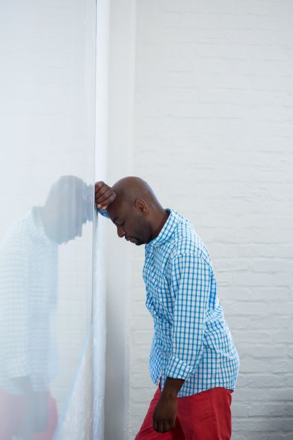 Upset man with eyes closed and hand on the forehead leaning against a wall in office