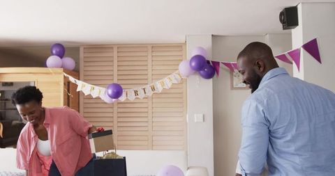 African american couple celebrating birthday at home, woman reaching into gift bag