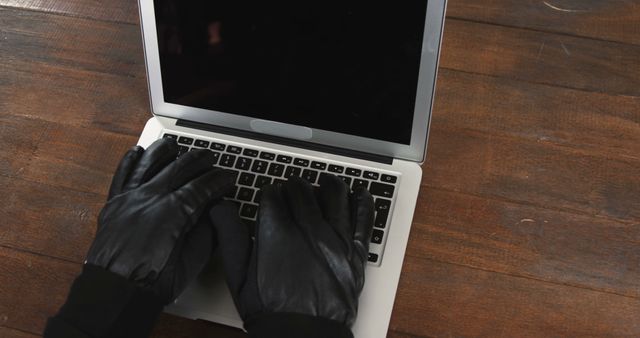 Hands wearing black gloves typing on a laptop keyboard. Perfect for themes related to cyber security, hacking, online safety, and technology. Could be used in articles about online threats, computer crimes, or technology precautions. The dark gloves create a mysterious and slightly menacing atmosphere.