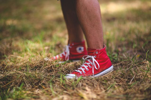 Person wearing red canvas sneakers. The ground is covered in dry grass, a pleasant day in nature. Perfect for themes related to casual fashion, outdoor activities, youth, and leisure. Useful for articles about footwear, walking, and outdoor exploration.