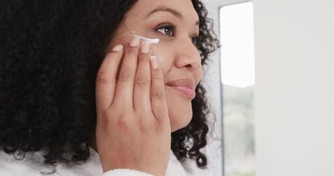 Applying moisturizer at vanity, woman using facial cream for glowing natural skin care