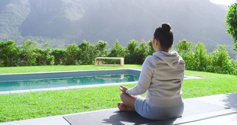 Asian Woman Meditating Outdoors Near Pool and Mountains