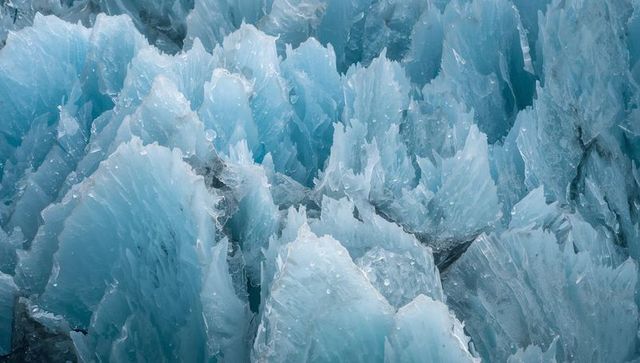 Jagged blue glacier ice spires close-up featuring meltwater droplets and crystalline pinnacles