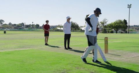 Cricket umpire beckoning batsman onto pitch during community match on sunny field