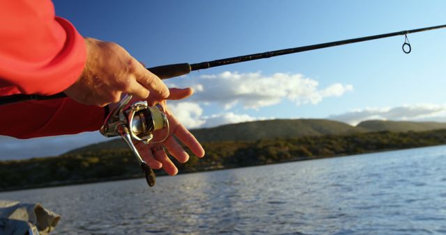 Close-up of a fisherman's hands holding a fishing rod, with copy space. Outdoor setting captures the essence of a tranquil fishing experience by the water.