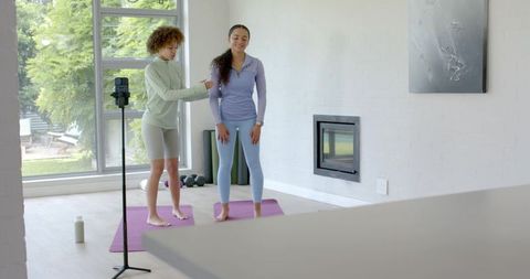 African american trainer coaching client during home yoga session filming on phone tripod