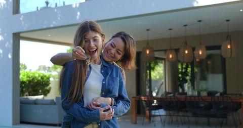 Joyful diverse female partners celebrating new home, holding key fob on sunlit patio