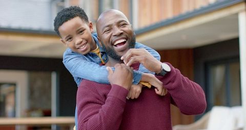 African american father carrying son on porch laughing, joyful family bonding outdoors