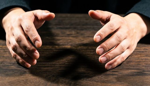 Hovering hands casting soft shadow over dark wood table, gesture and mood lighting