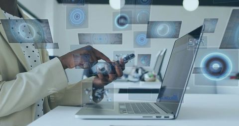 Businesswoman using smartphone with holographic data interface over laptop in modern office