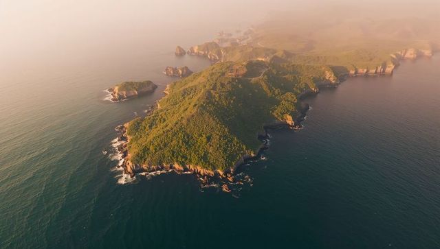 Sunlit rugged headland stretching into misty ocean with sea stacks and surf lines