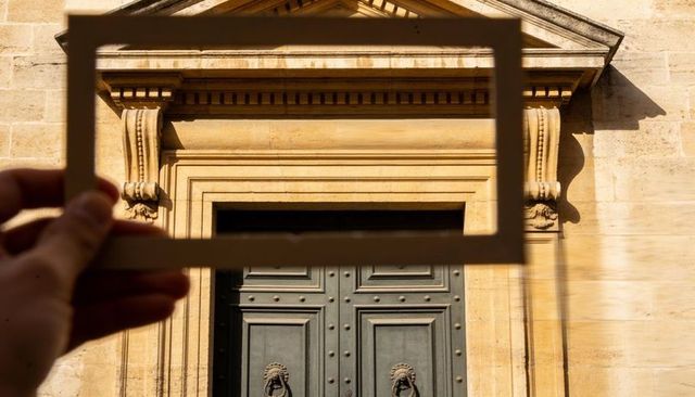 Hand holding wooden frame framing ornate classical doorway in warm golden sunlight