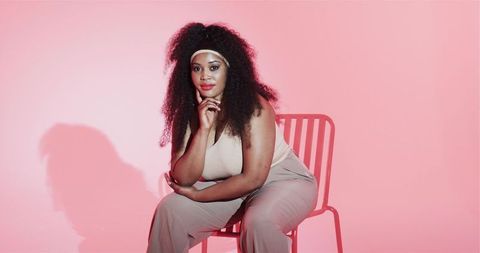 Confident Woman Sitting on Chair with Pink Studio Background