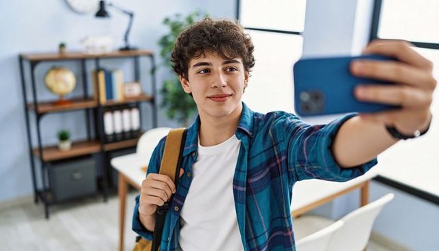 Teenage student taking selfie in bright study room with backpack and smartphone