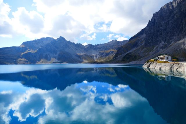 Idyllic mountain lake with crystal-clear blue water mirroring the sky and clouds. Surrounded by rugged rocky mountains, this serene alpine landscape is perfect for travel promotions, nature wallpapers, and environmental awareness campaigns.