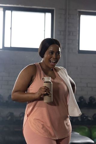 African american woman smiling and holding water bottle after workout in gym studio