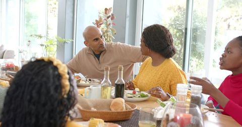 Multigenerational Black Family Sharing Sunlit Meal Around Wooden Table During Conversation