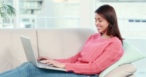Asian Woman Smiling While Using Laptop on Sofa