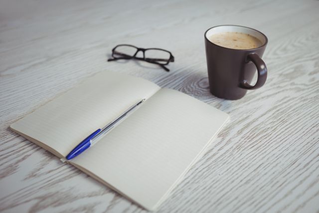 High angle view of pen and book with coffee cup on table 