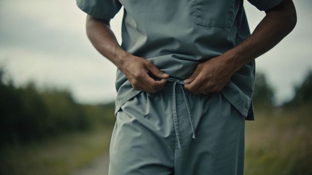 Adjusting scrub pants, tying drawcord on outdoor trail by medical worker