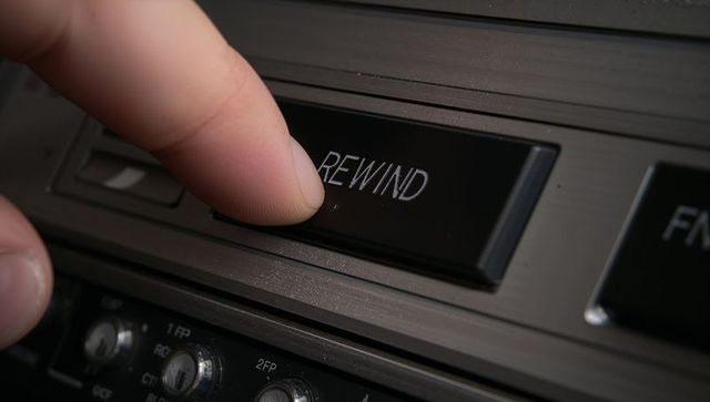 Finger pressing rewind button on vintage metal cassette deck close-up for retro audio use