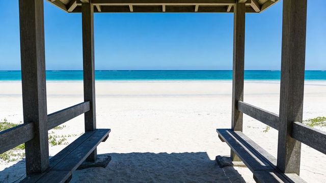 Wooden beach shelter framing turquoise ocean and pristine white sand with shaded benches