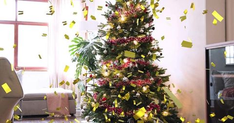 Cozy living room christmas tree glowing with red garland and falling gold confetti
