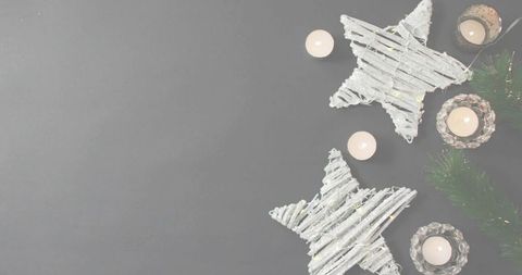 Rustic woven star ornaments and candlelight on neutral gray background with copy space