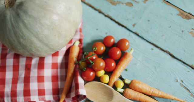 This image showcases a selection of fresh vegetables, including cherry tomatoes, baby carrots, and a pumpkin, on a rustic turquoise table. A red checkered cloth adds a pop of color, and a wooden spoon enhances the farm-to-table theme. This vibrant, rustic scene is perfect for marketing healthy eating, organic produce, and farm-to-table lifestyle. It can also be used in cooking blogs, recipe books, and advertisements for farmers' markets or organic brands.