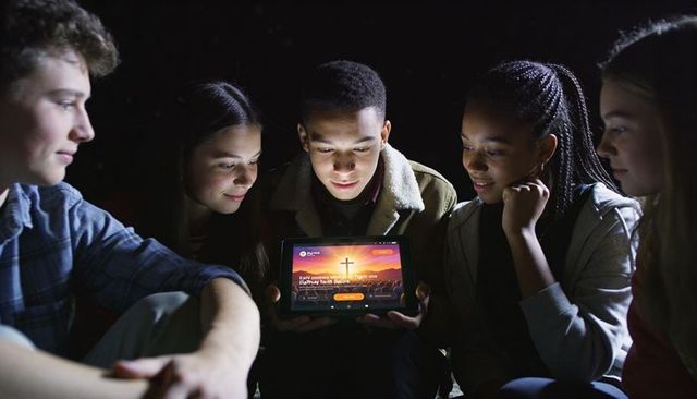Multiracial teens gathering around tablet nighttime viewing glowing cross app