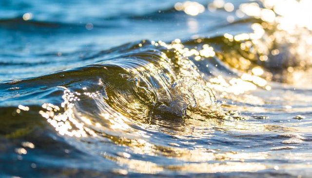 Golden sunlight dancing on glassy cresting wave casting sparkling ripples and amber glow