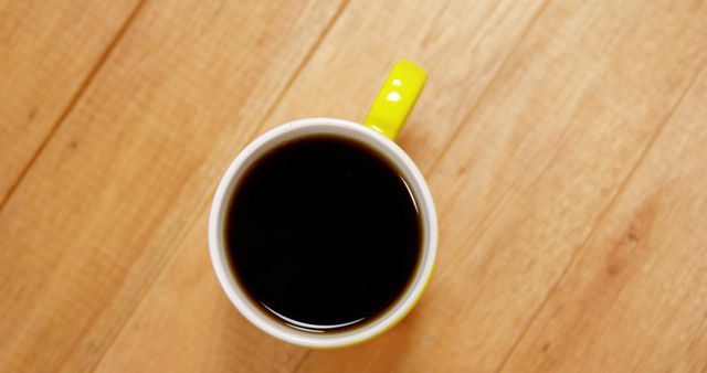 A top view of a full cup of coffee with a yellow handle on a wooden surface, with copy space. Coffee is a popular beverage enjoyed globally for its stimulating effects and rich flavor.