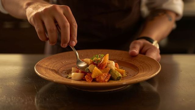 Plating gourmet vegetable medley by chef adjusting microgreens on rustic ceramic plate