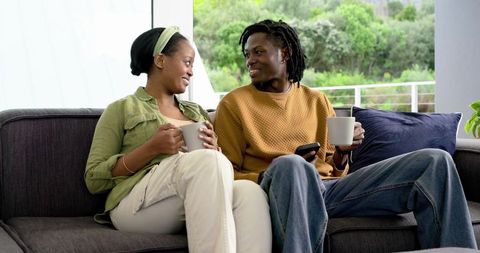 African American couple sharing coffee and conversation on sofa by balcony with greenery