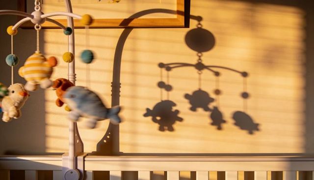 Sunlit crib mobile casting playful plush shadows across nursery wall during golden hour