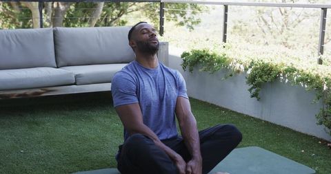 Mature man practicing deep breathing and meditating on balcony yoga mat