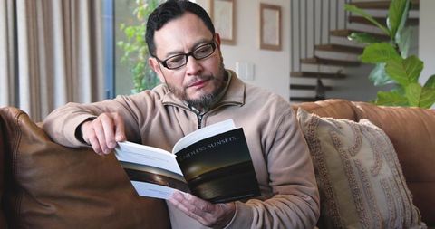 Mature asian man relaxing on sofa reading book at home