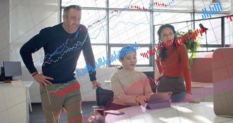 Diverse team analyzing market charts on tablet and phone in bright modern office