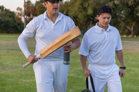 Cricket teammates walking off field carrying wooden bat and kit bag during golden hour