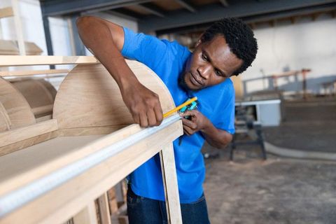 African american craftsman measuring wood frame with tape measure making furniture