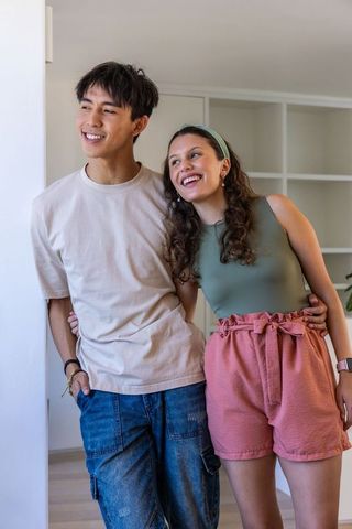 Young diverse couple leaning in doorway, smiling and showing smartwatch in cozy interior